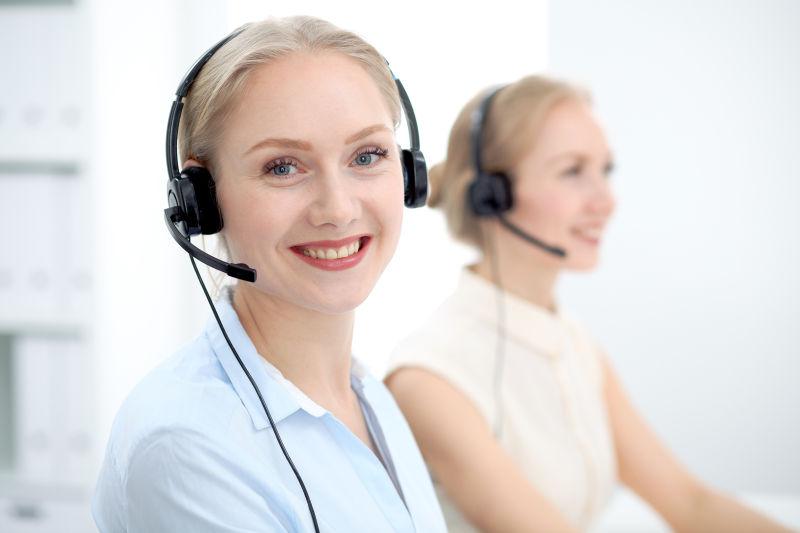 Two customer service representatives smiling while answering client calls, symbolizing quality service and reliable support in the amusement rides industry.